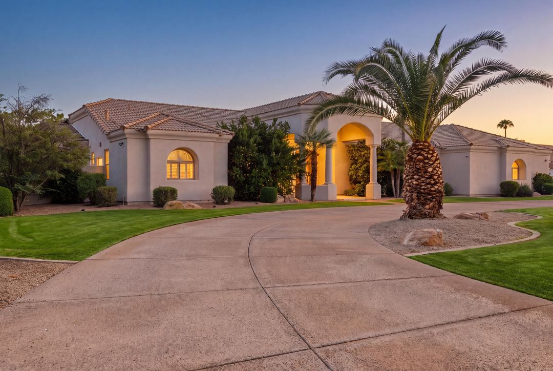 Mediterranean estate at dusk behind a curved drive and a tall palm