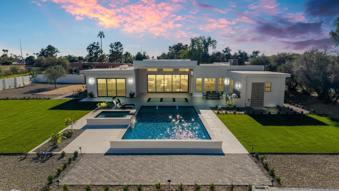 Glass-walled modern home behind a lit pool at dusk