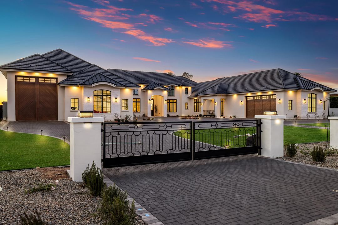 Gated estate at dusk with wood garage doors and every window lit