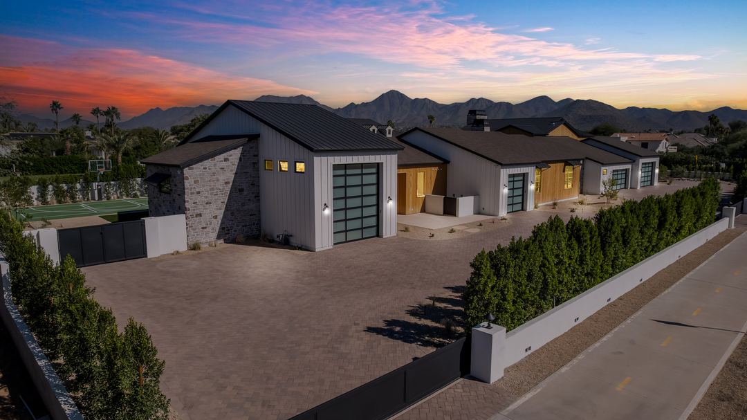 Twilight aerial of a modern estate with a lit pool and pickleball court