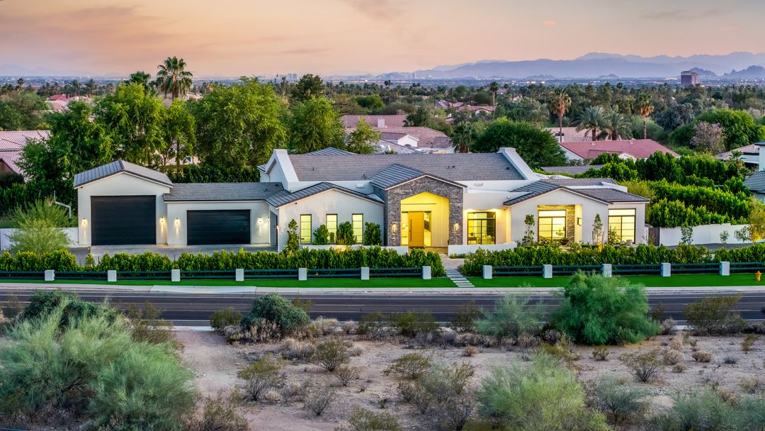 Twilight aerial of a modern farmhouse with a stone entry, lit from inside, with the Valley and mountains behind